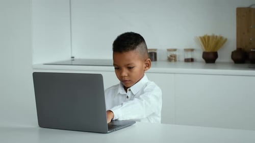 Young Boy Focused on Laptop at Home During Schoolwork in a Modern Kitchen