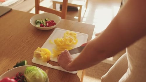 Nahaufnahme der Hände einer jungen Frau, die zu Hause in der Küche Paprika schneidet und Salat zubereitet
