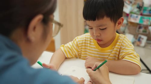Asian child boy student concentrating on drawing activity with mother