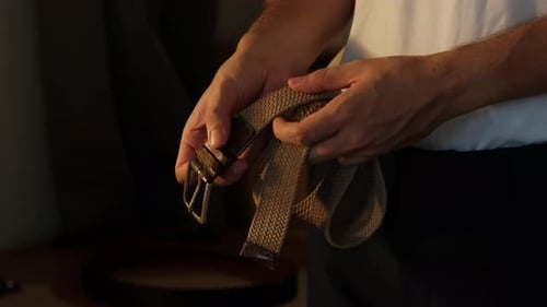 Close-Up of Man Putting On and Fastening Fabric Belt Indoors