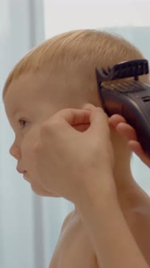 Vídeo vertical: Una joven madre le da a su hijo un elegante corte de pelo en casa con un cortaúñas