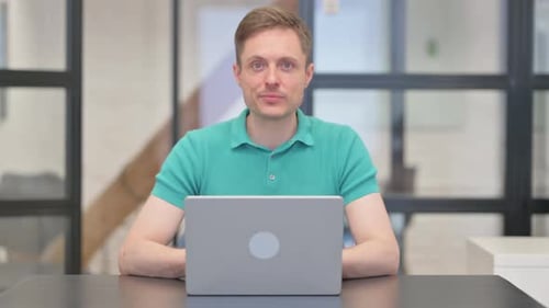 Mature Adult Man Pointing at Camera while Using Laptop
