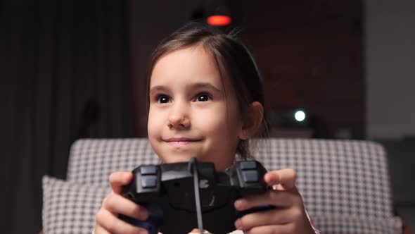 Niña jugando videojuegos en casa y sosteniendo un controlador sonriendo ...