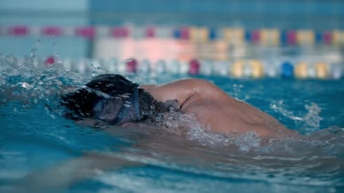 Nadador musculoso con gafas entrena estilo libre en el agua de la piscina