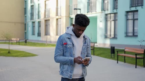 Smiling African American Man Standing on City Street with Modern Smartphone in Hands Positive Young