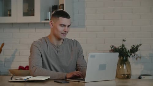 A Young Businessman in a Gray Sweatshirt Works Productively at His Laptop While Sitting in His Home
