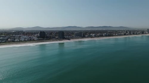 Drone clip over calm ocean showing a very built up coastal city and long stretch of beach