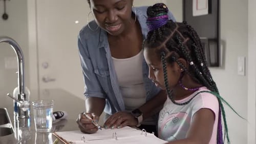 Woman Helping Young Girl Draw in Kitchen