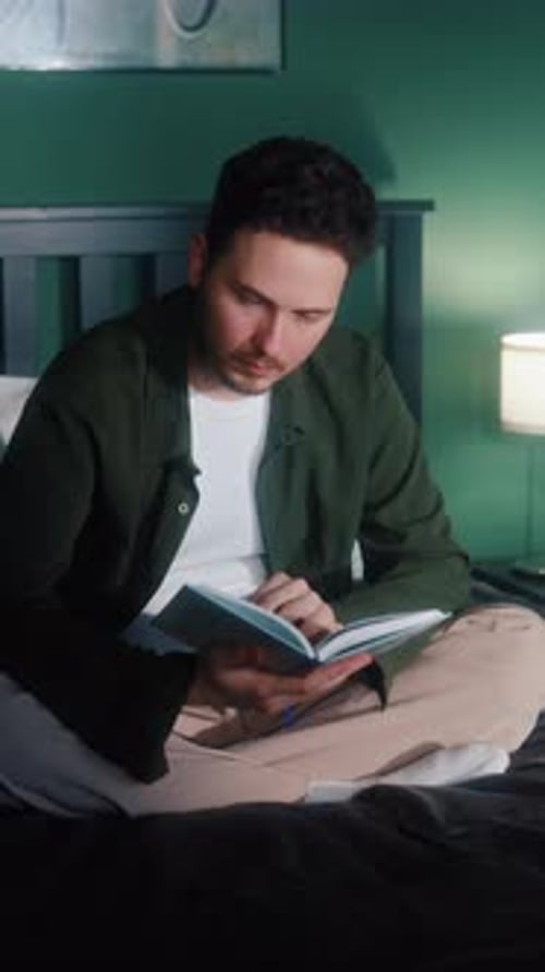 Man Reading Book in Bed Near Night Lamp