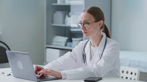 Female Doctor Working on Laptop and Taking Notes in Modern Medical Office