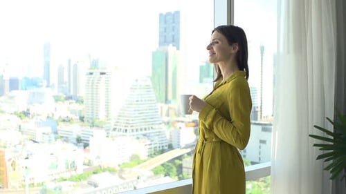 Young Woman with Beverage Admire View From Window at Home 30s