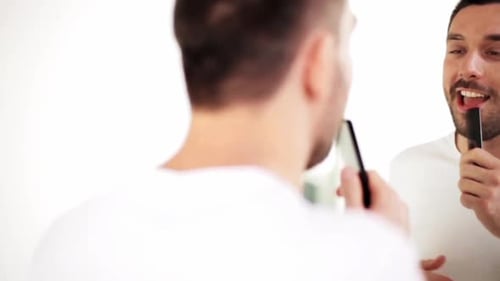 Smiling Man Combing Beard in Bathroom Mirror