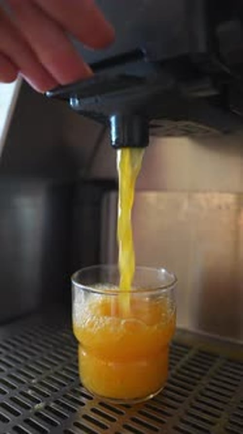 Gros plan d'une machine à jus de fruits frais distribuant du jus d'orange dans un café