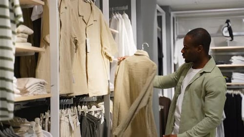 Un client afro-américain choisit des vêtements dans un magasin de mode avec réduction