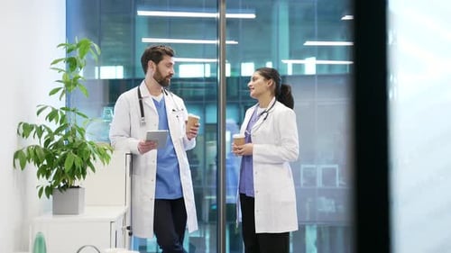 Two colleagues doctors engaged in friendly conversation with coffee in modern hospital office.