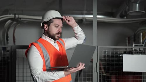 Electrical Engineer Works on Laptop Next to Electrical Control Panel in Industrial Setting