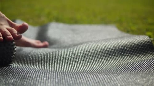 Young Woman Doing Myofascial Release for Feet Using a Little Ball on the Sport Mat on Green Grass