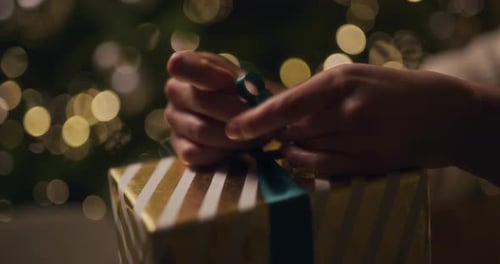 Hands Untying Christmas Gift Ribbon at Night