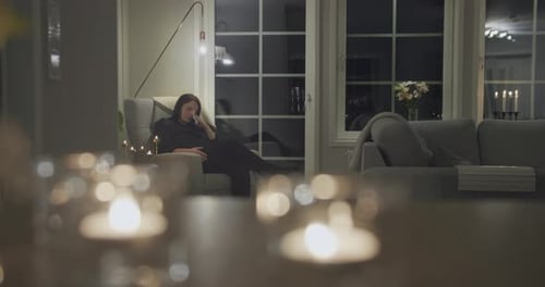 Woman Sits in Chair in Living Room at Night
