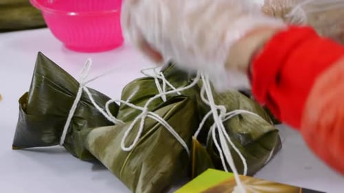 Bunch of Asian rice triangles wrapped in leaf tied together with string and placed on table filmed a