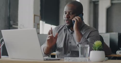 Ambitious African American Man Talking on Mobile Phone and Using Laptop Working in Office