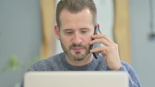 Close Up of Mature Adult Man Talking on Phone while using Laptop