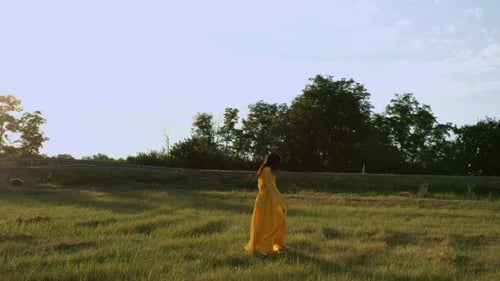 Drone Filming of Young Girl in Yellow Dress Running on Meadow Towards Road Slow Motion