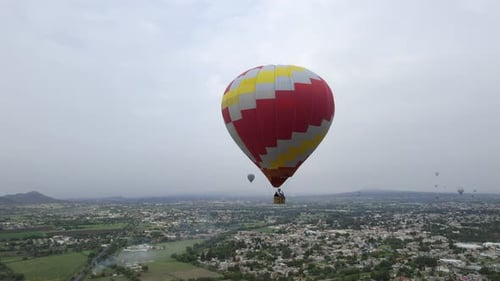Tourists in a hot air balloon flying over a city on a cloudy day - Aerial view