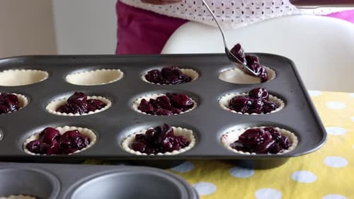 Femme préparant des tartes aux cerises, remplissant des moules à pâtisserie de compote de cerises. Mouvement lent