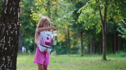 Girl playing outdoor. Happy little girl blowing soap bubbles in park