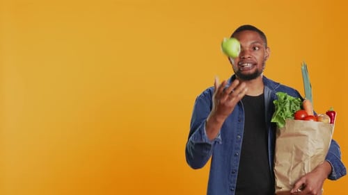 Hombre seguro haciendo malabares con una manzana verde ecológica frente a la cámara