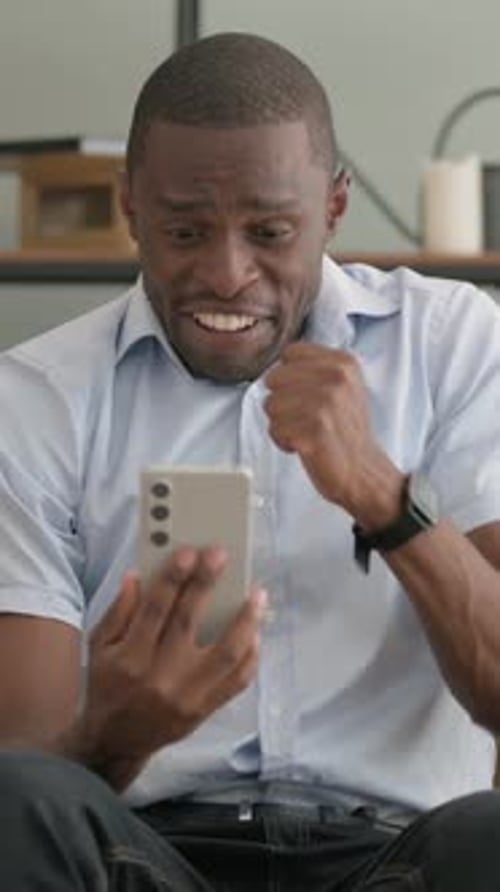 Young Man Excitedly Celebrates While Using Smartphone