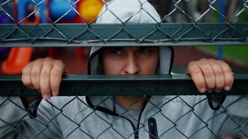 Portrait of a Criminal Man or a Bandit in a Hood Looking Through the Fence Bars