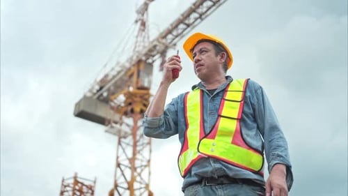 Portrait d'un grutier utilisant un talkie-walkie pour communiquer avec les opérateurs de grues à tour pour soulever et déplacer
