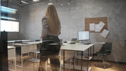 A Female Instructor Walking Through a Modern Office with Transparent Walls Observes Her Students