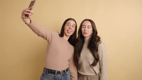 Friends Posing Playfully for a Selfie Against a Beige Background