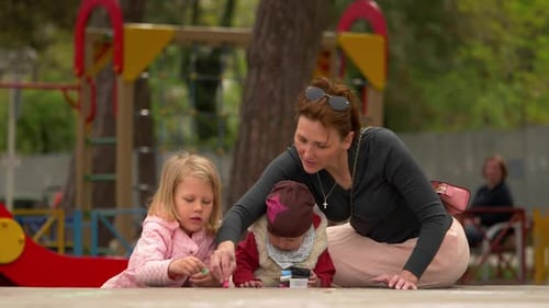 junge Mutter mit ihren Kindern auf dem Spielplatz spielt mit farbigen Kreiden