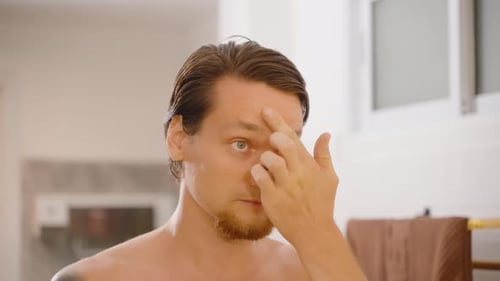 Man Applying Face Cream on Forehead in Bathroom Mirror, close angle, Male Skincare Concept