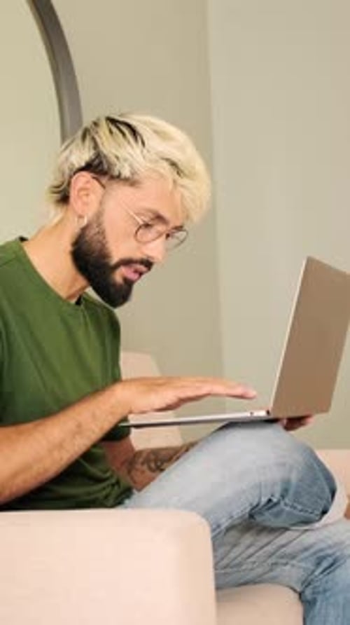 Young blond man with a beard works on a laptop while sitting in a cozy living room