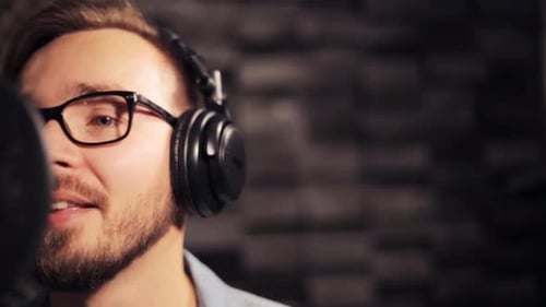 Male singer with headphones and microphone singing song at recording studio