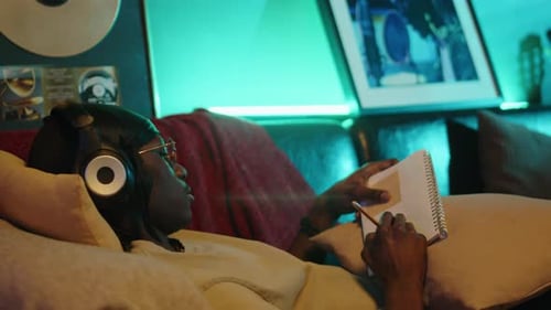 Musician Relaxing on Sofa and Writing Lyrics in Notebook