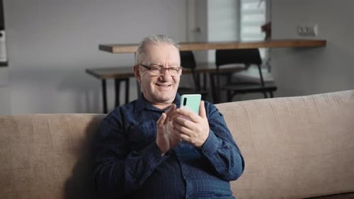 Senior Man Using Smartphone on Couch at Home