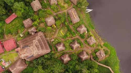 Verdant Foliage Framing Wooden Eco Lodge with Thatched Roofing Perched Beside Dark River Waters