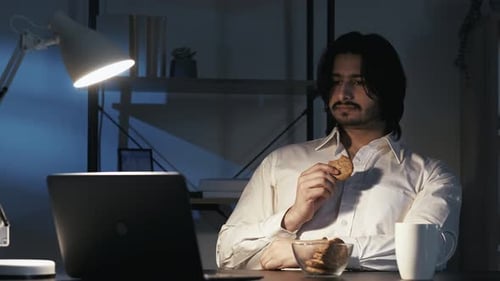 Young Adult Man Eating Cookies While Working