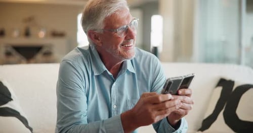 Senior Man Using Folding Smartphone on Couch Indoors