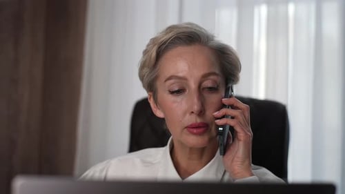 Closeup of Mature Adult 50s Businesswoman Talking Phone Typing Laptop Multitask in Office Portrait