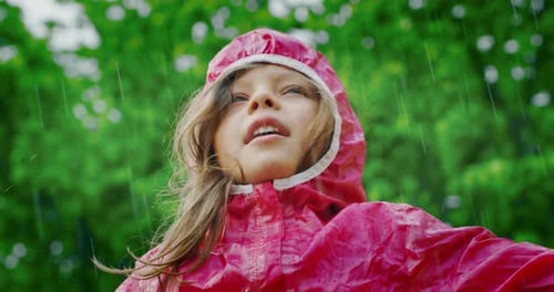 Authentic shot of carefree happy little girl in raincoat is having fun and enjoying the rain in a