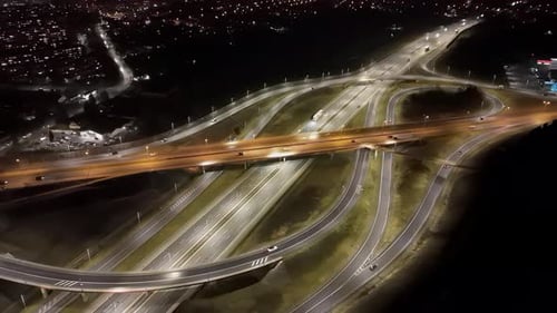 Aerial View of Illuminated Highway Interchange at Night with Flowing Traffic and Surrounding City