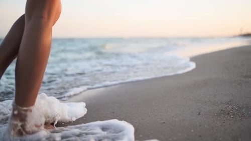 Slim Female Legs and Feet Walking Along Sea Water Waves on Sandy Beach Pretty Woman Walks at Seaside