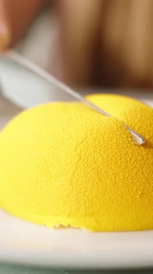 Vertical video. A woman slowly cuts a lemon mousse dessert in half, close-up.